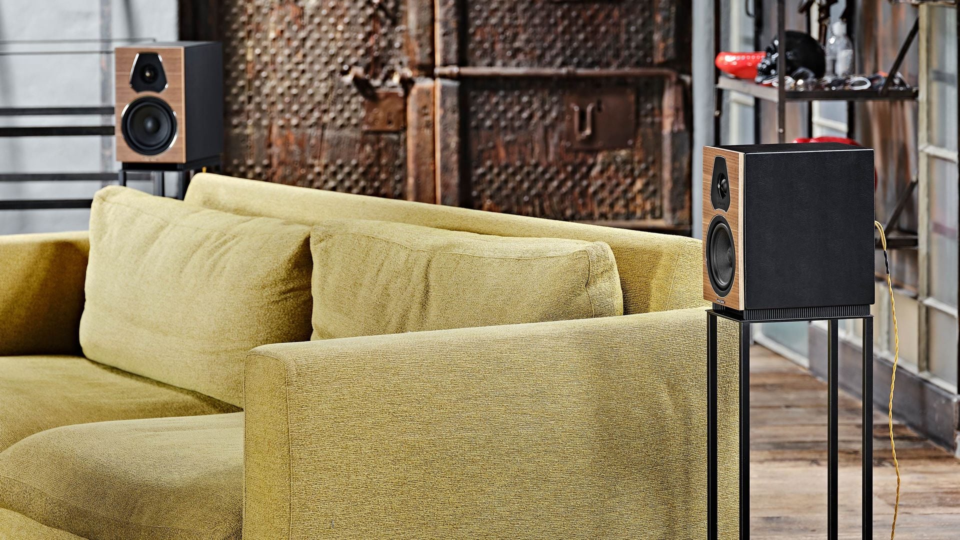 Dúo de altavoces de estantería Lumina II elegantemente ubicados sobre soportes, enmarcando un sofá para una experiencia de escucha de audio envolvente en el hogar.