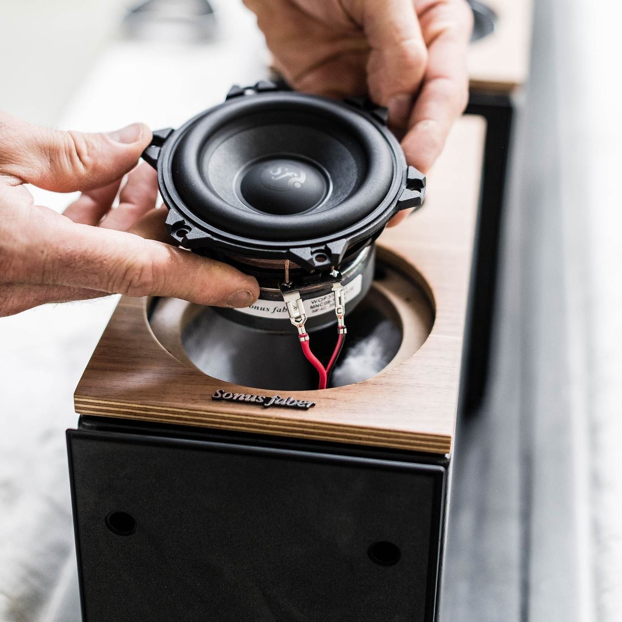 Un artesano italiano de Sonus faber coloca con destreza el altavoz de medios de un altavoz de estantería Lumina II, demostrando habilidad y artesanía.